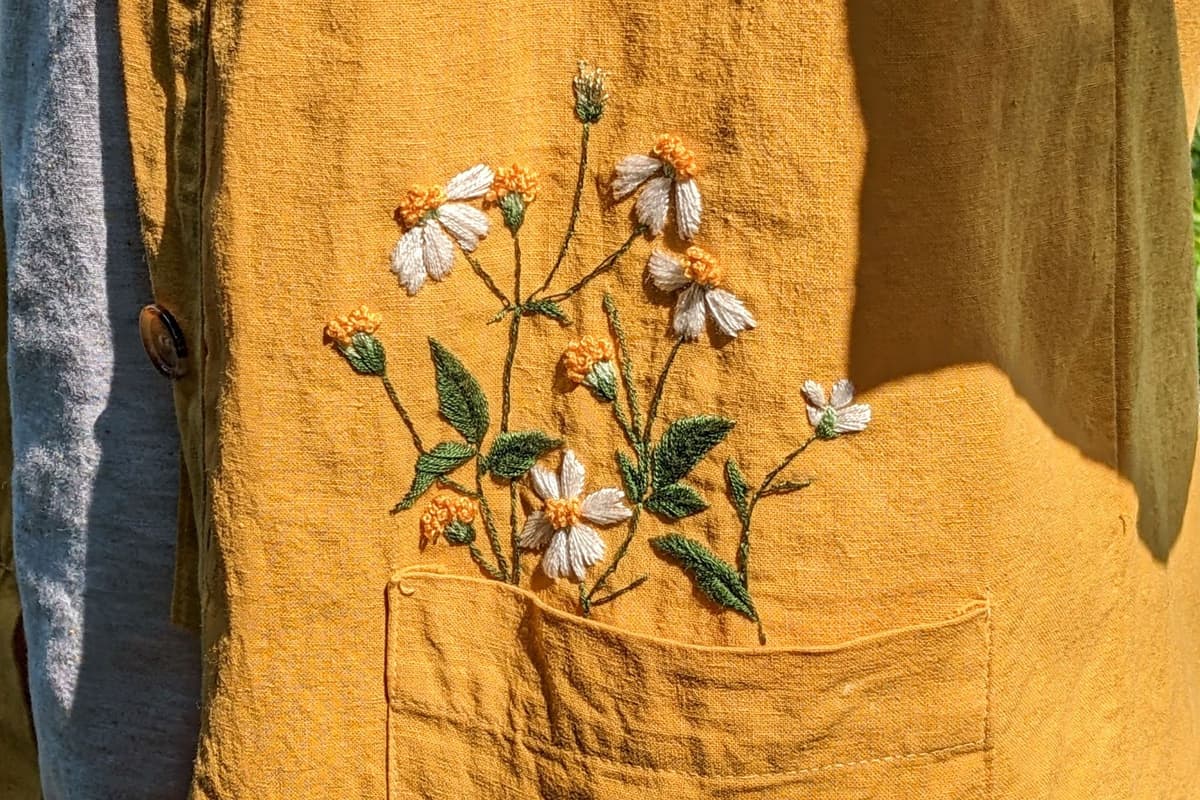 Embroidered daisies stitched into a linen pocket, close enough to see the raised thread