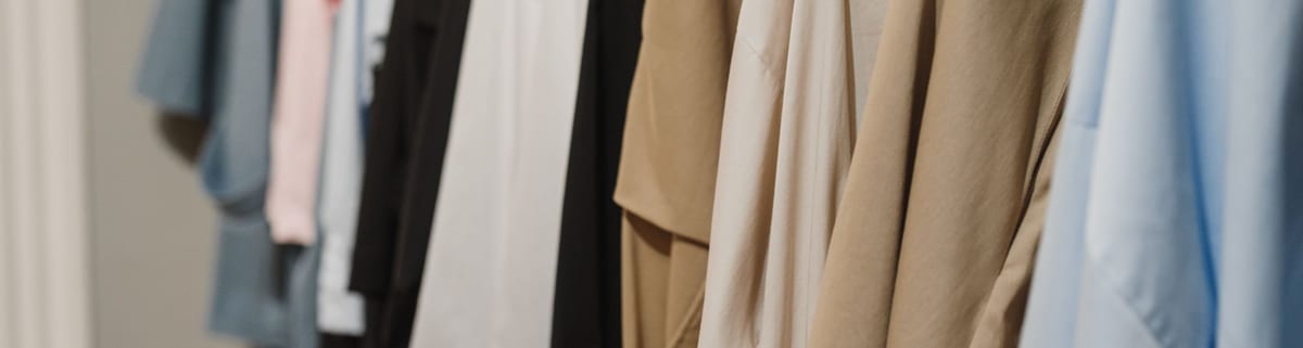 Clothing rail packed with plain shirts and tops in tan, cream, black and pale blue, photographed close in so the garments fill the frame