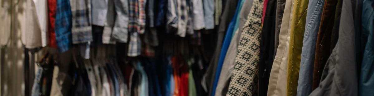 Clothing rails packed with shirts, knitwear and trousers, photographed close in so the garments fill the frame