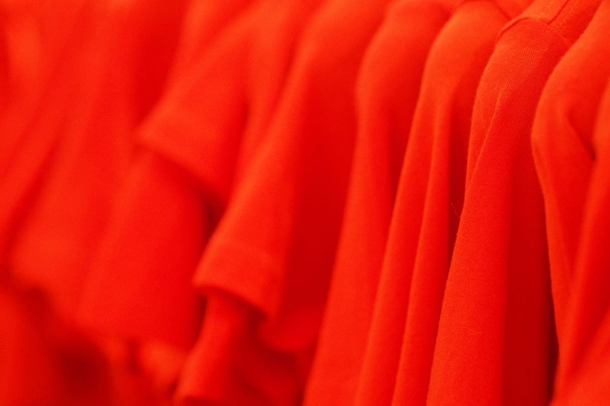 A row of identical red t-shirts hanging on a rack, each one the same shade and cut