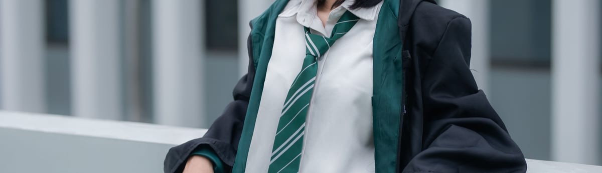 School uniform with a white collared shirt, a green and white striped tie and a dark blazer, the school crest stitched at the base of the tie