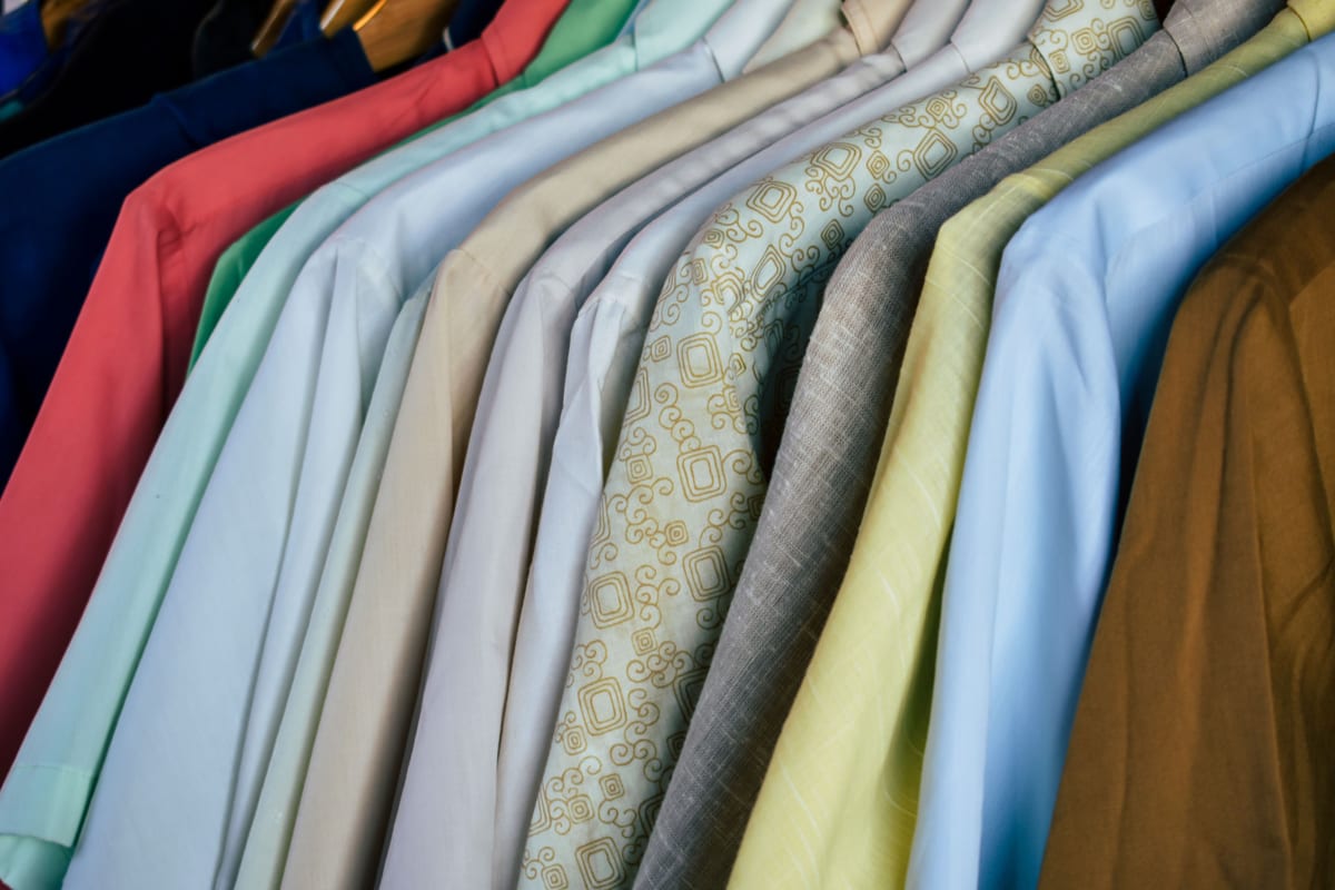 Button-front shirts in a range of colours hanging side by side on wooden hangers