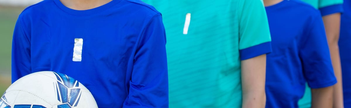Young team players standing in a row in plain blue and teal jerseys, photographed close in across the chest