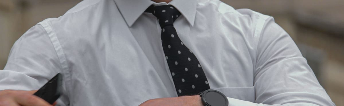 White business shirt with a spread collar and a black polka-dot tie, photographed close in across the chest and forearms