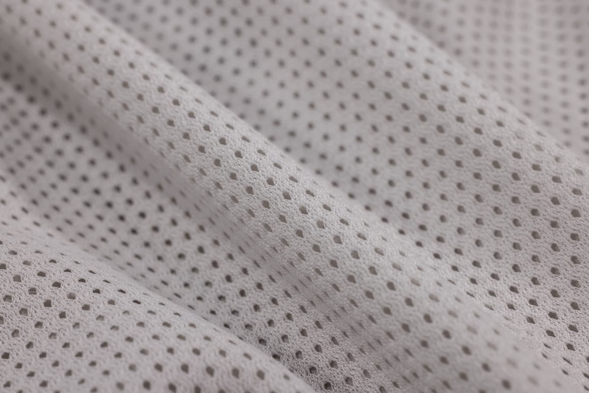 Close-up of white performance mesh fabric, folded, with rows of small vent holes through the knit